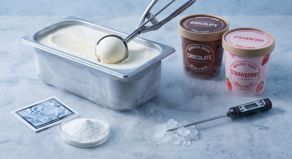 Smooth creamy reduced sugar ice cream being scooped beside soluble tapioca fiber powder thermometer and ice crystal microscope card on chilled surface
